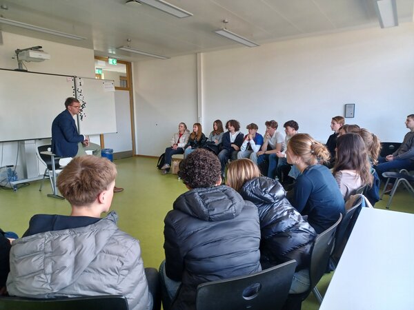 Sebastian Schmidt setzt sich mit einer Schülergruppe auseinander, die in einem Sitzkreis sitzen.