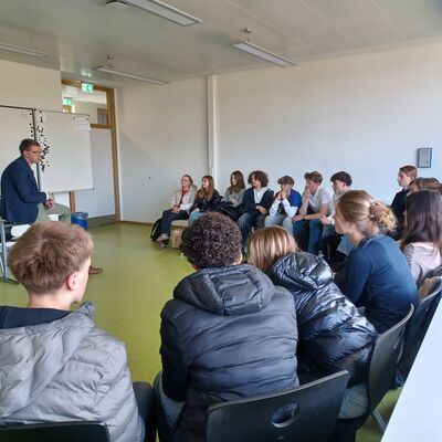 Sebastian Schmidt setzt sich mit einer Sch&uuml;lergruppe auseinander, die in einem Sitzkreis sitzen.