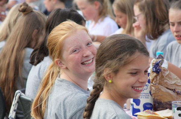Gruppe von Kindern mit Zöpfen und hellen Haaren sitzt an einem Tisch mit Getränken und Essen